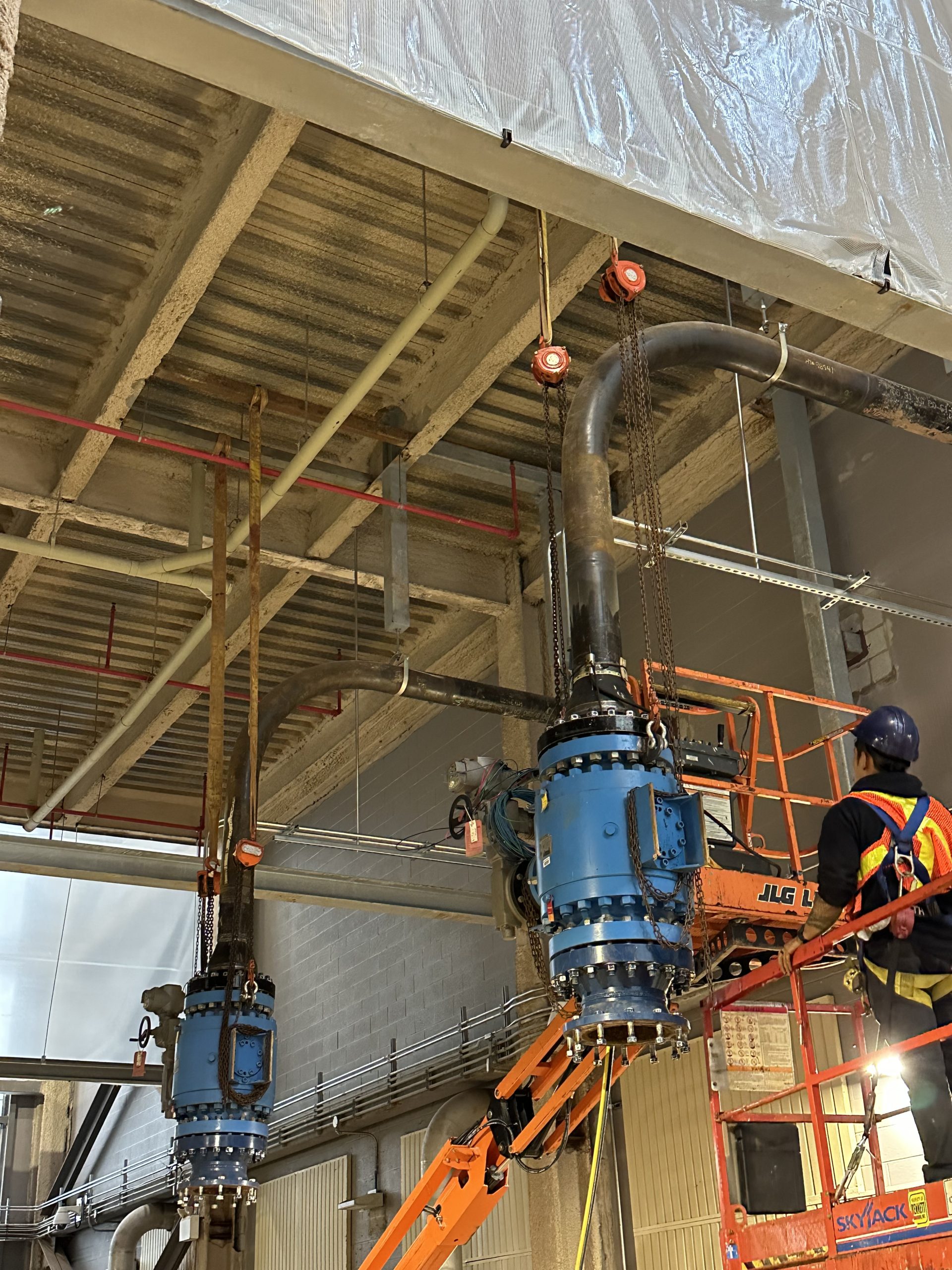 A worker in a factory setting is engaged with machinery and electrical cables.