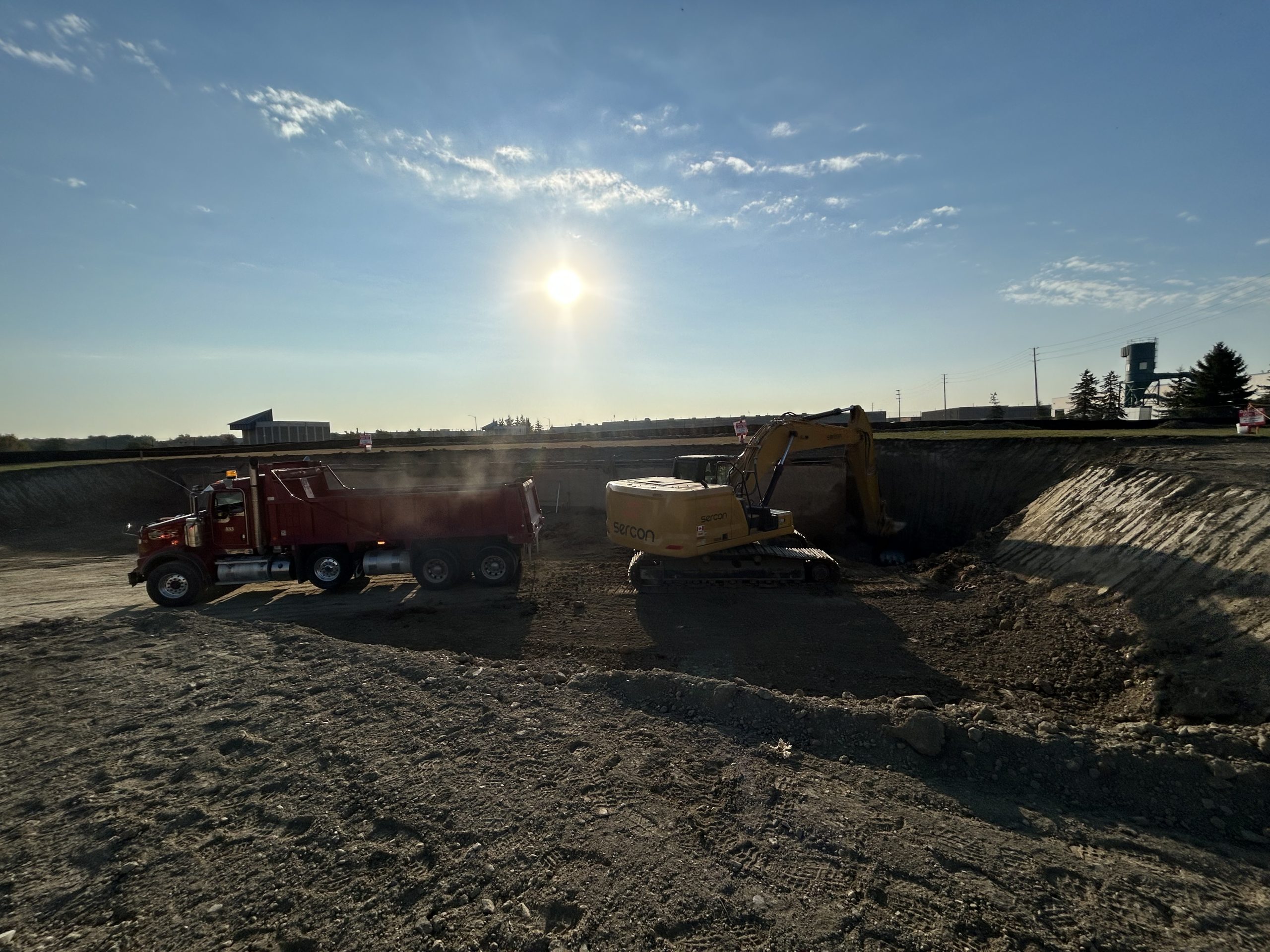 A heavy construction truck is parked on a construction site, surrounded by soil and equipment.